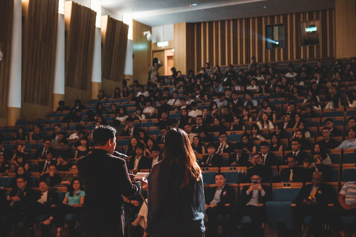 A university lecture hall, the scheduled setting where a device on the desk beats a worn pendant