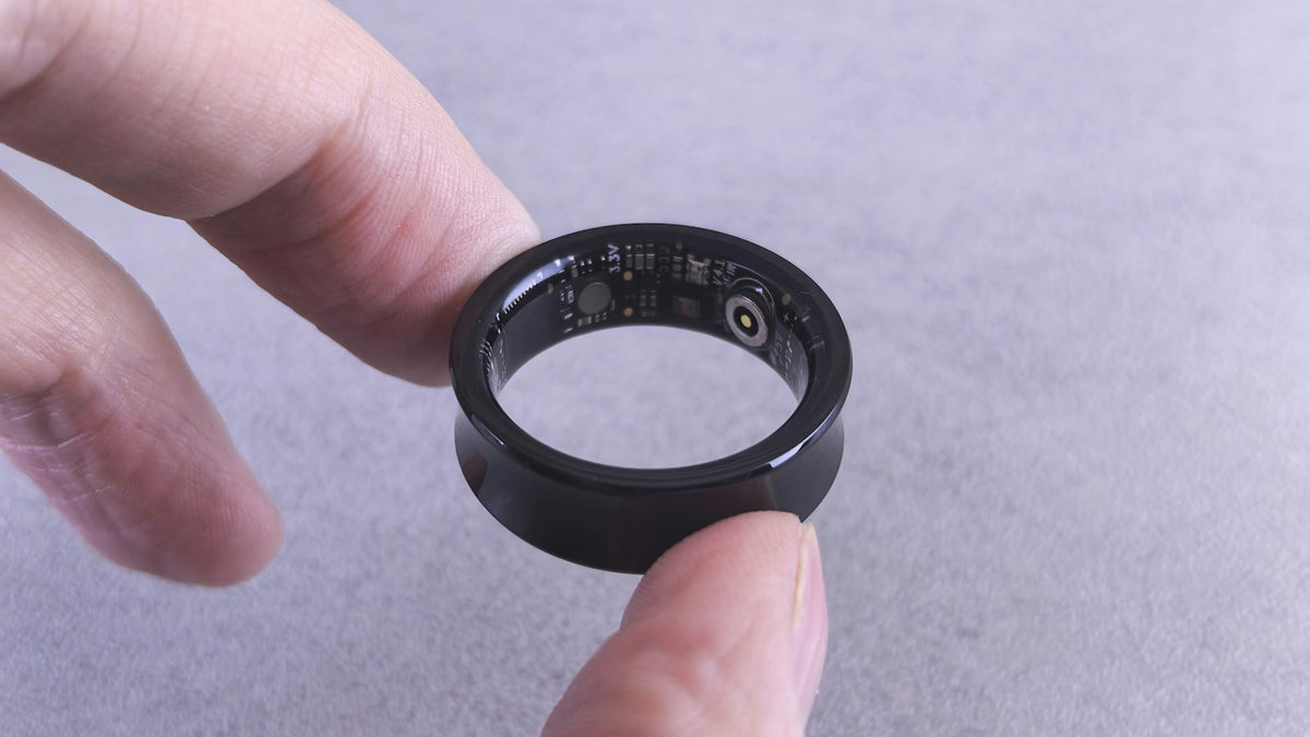 A wearable AI ring device with visible circuitry, held between two fingers