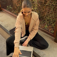 A woman sits cross-legged on a concrete ledge, working on a silver laptop