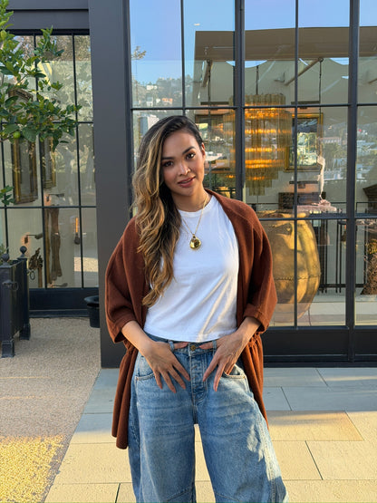 Woman wearing gold Legend One AI memory pendant with white t-shirt and jeans, standing outdoors in front of glass building, full-body lifestyle photo
